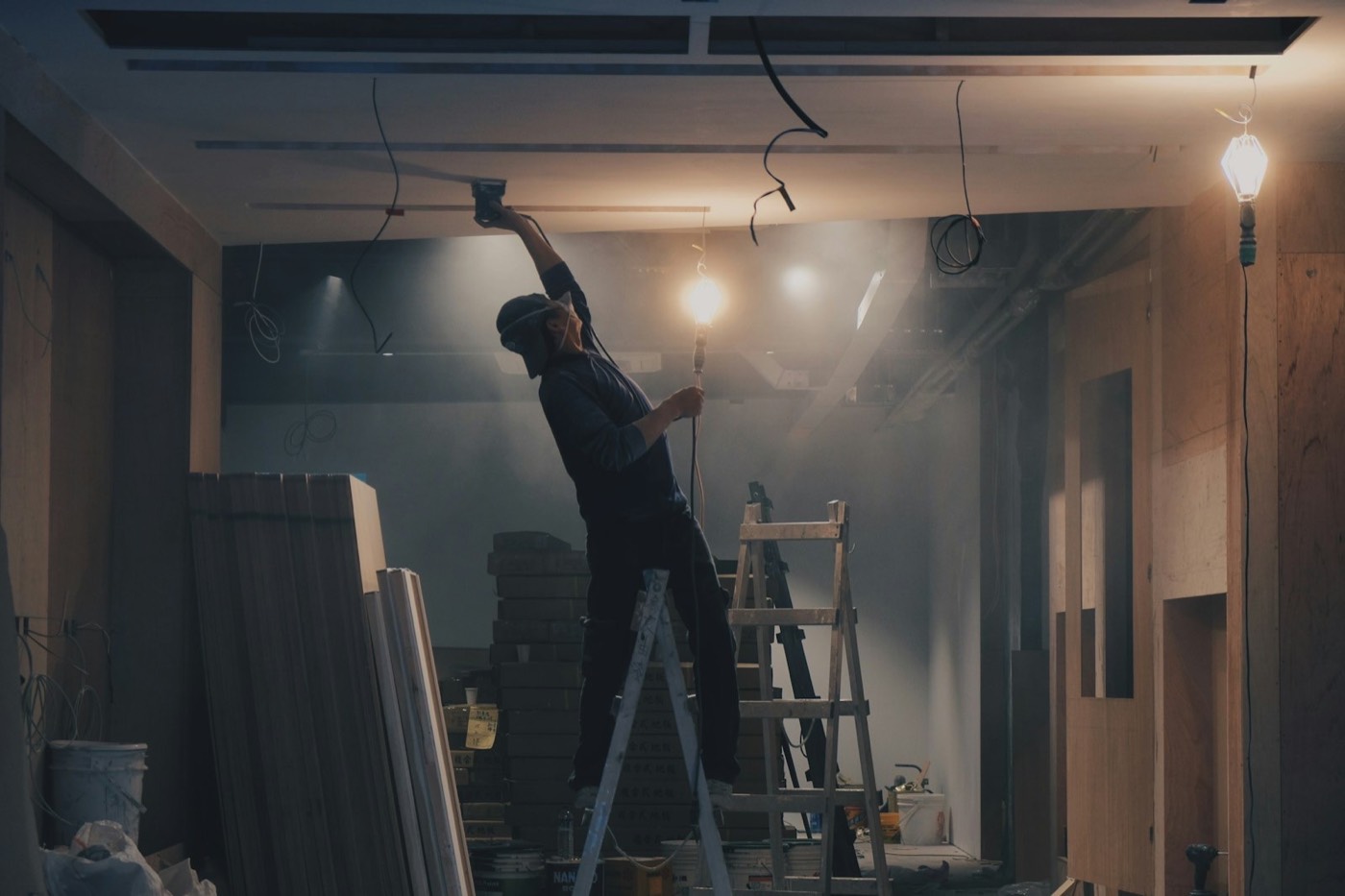 A worker on a ladder fitting a ceiling light in a room being renovated