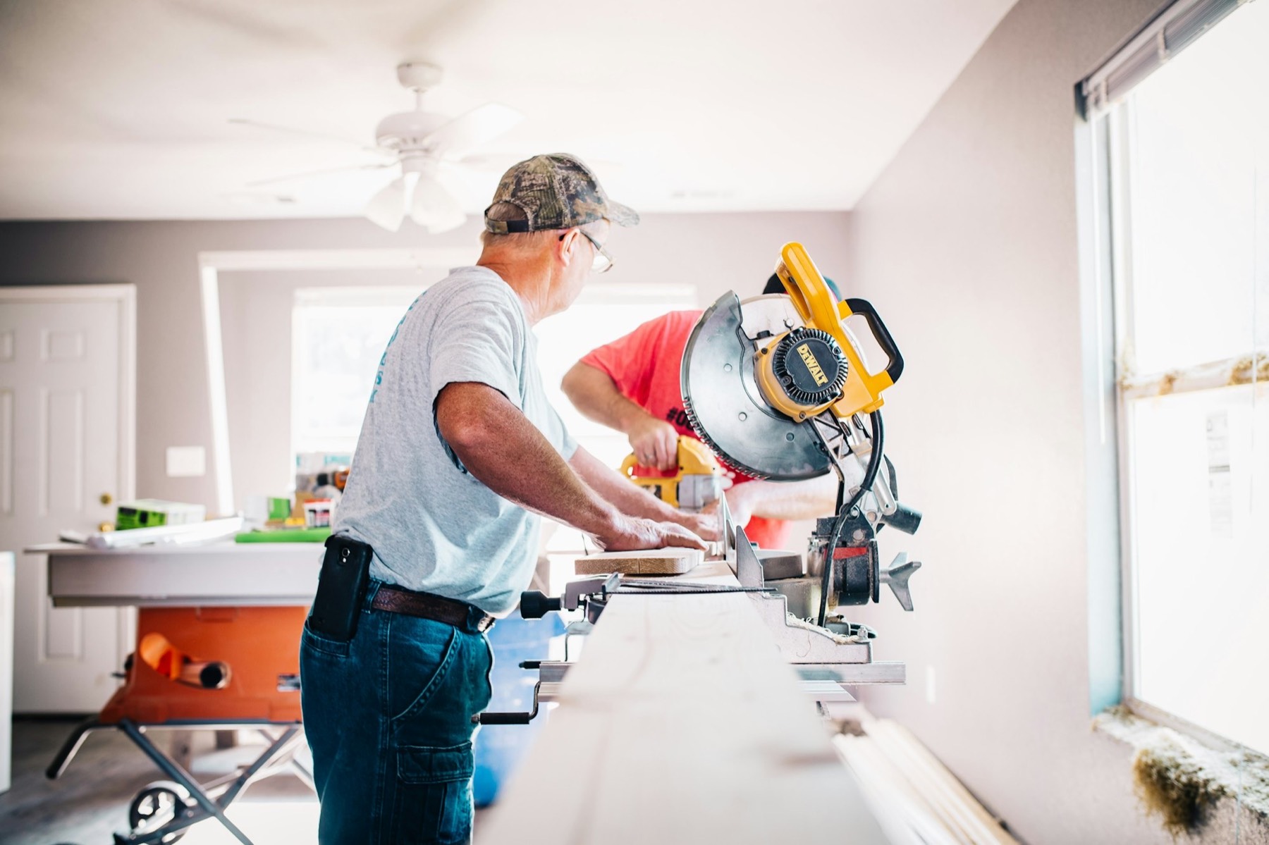 A carpenter cutting trim on a mitre saw in a bright room under renovation