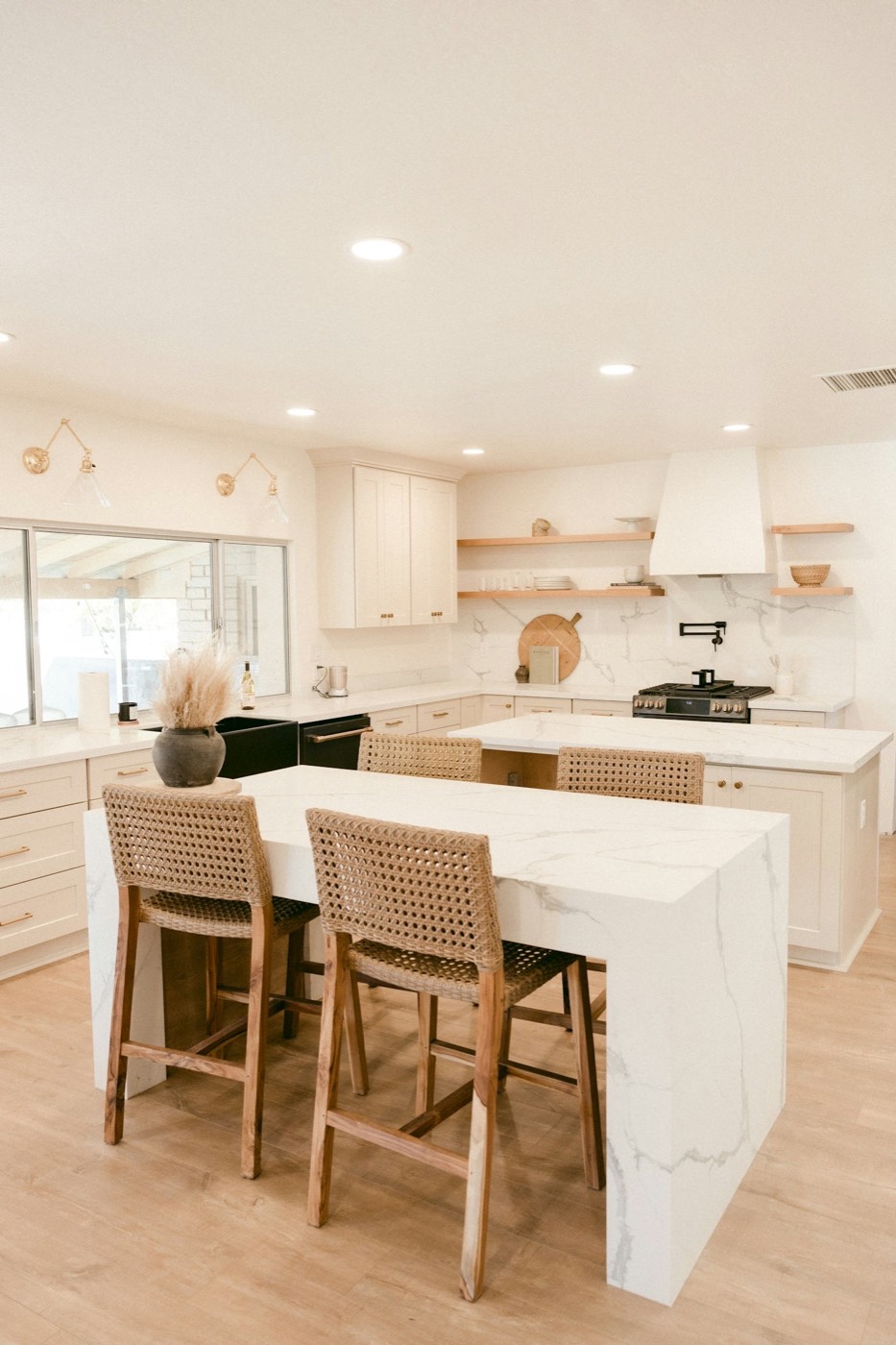 A kitchen with a marble island, wicker stools and open shelving