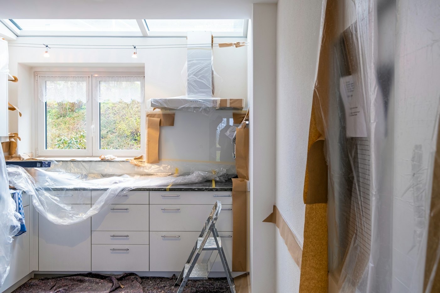 A kitchen under renovation with plastic sheeting and new white cabinets