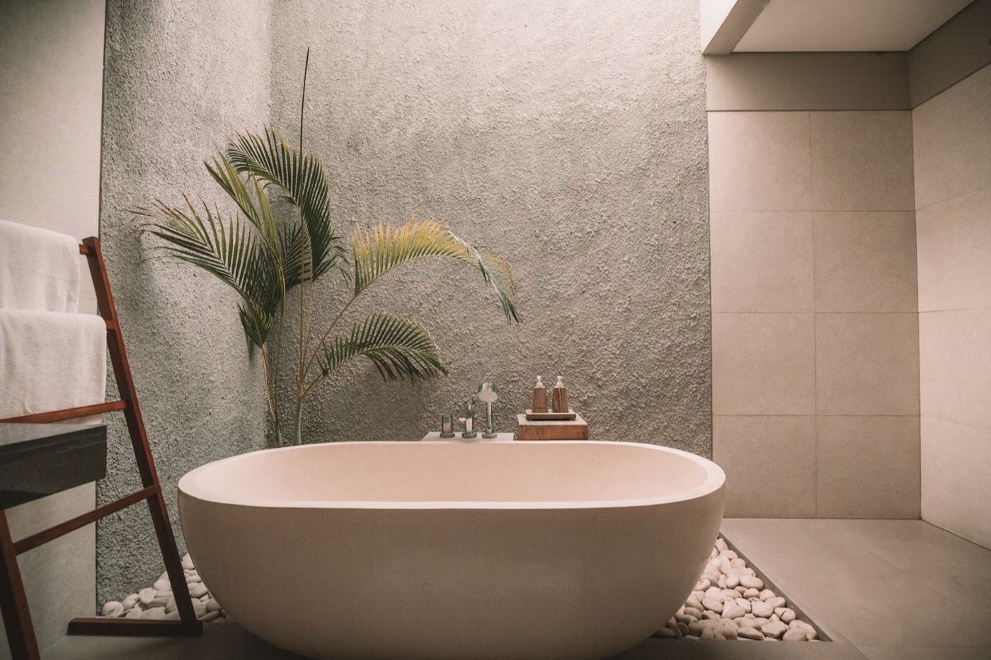 A freestanding tub in front of a textured plaster wall with a palm beside it