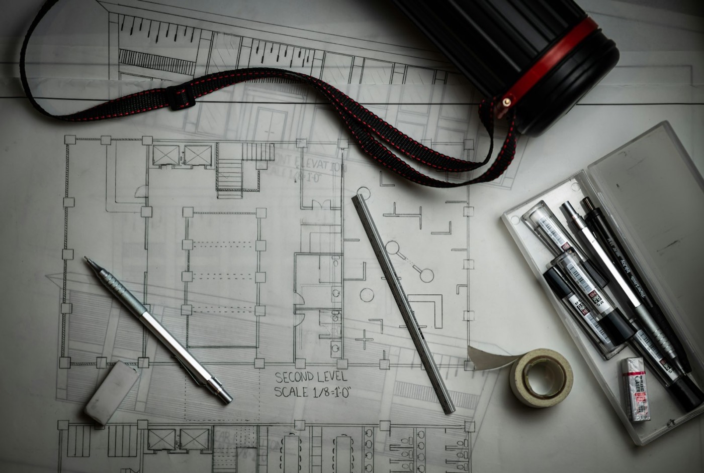 Architectural drawings on a desk with pens and a measuring tape