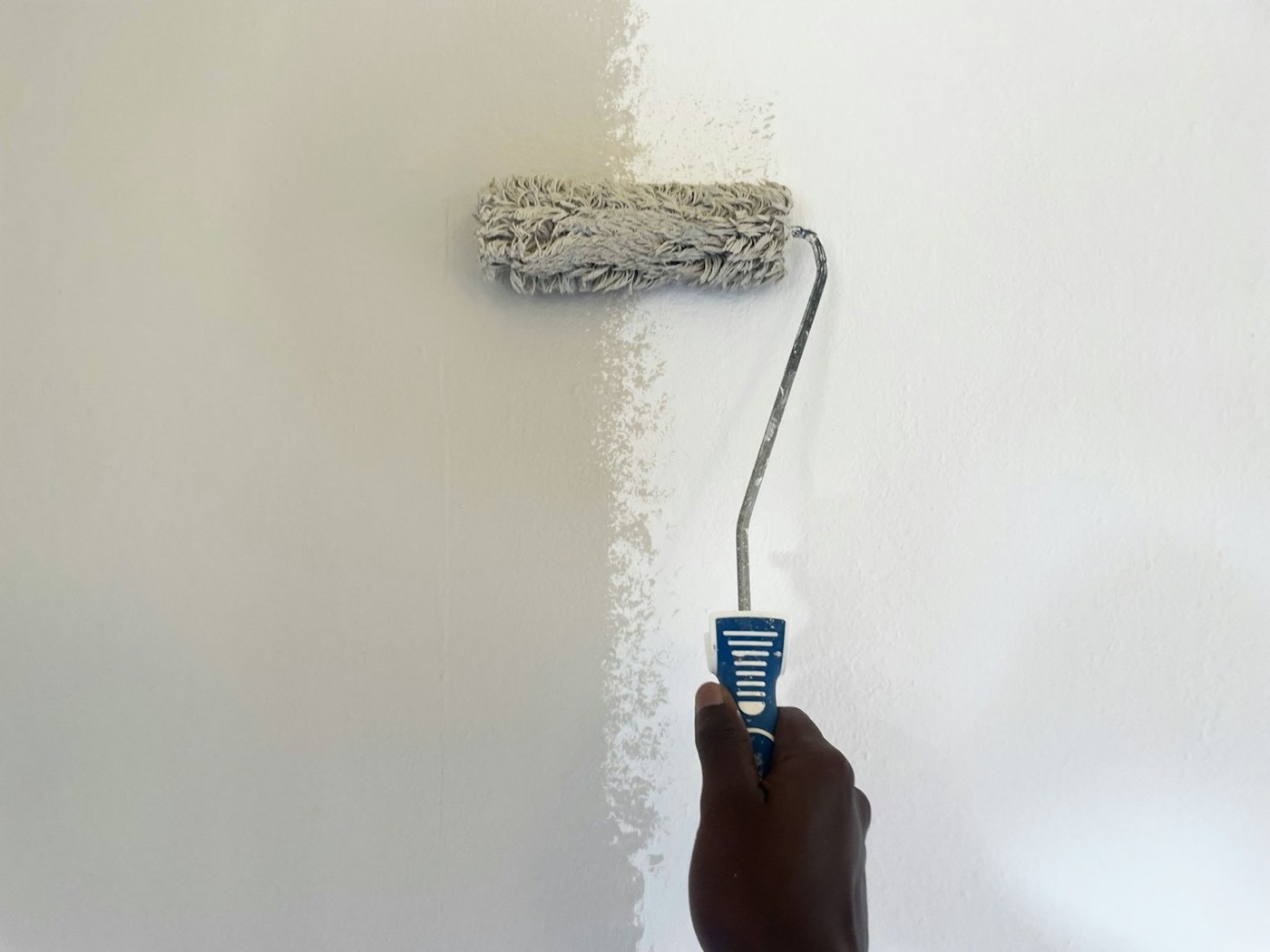 A paint roller rolling white paint onto a wall