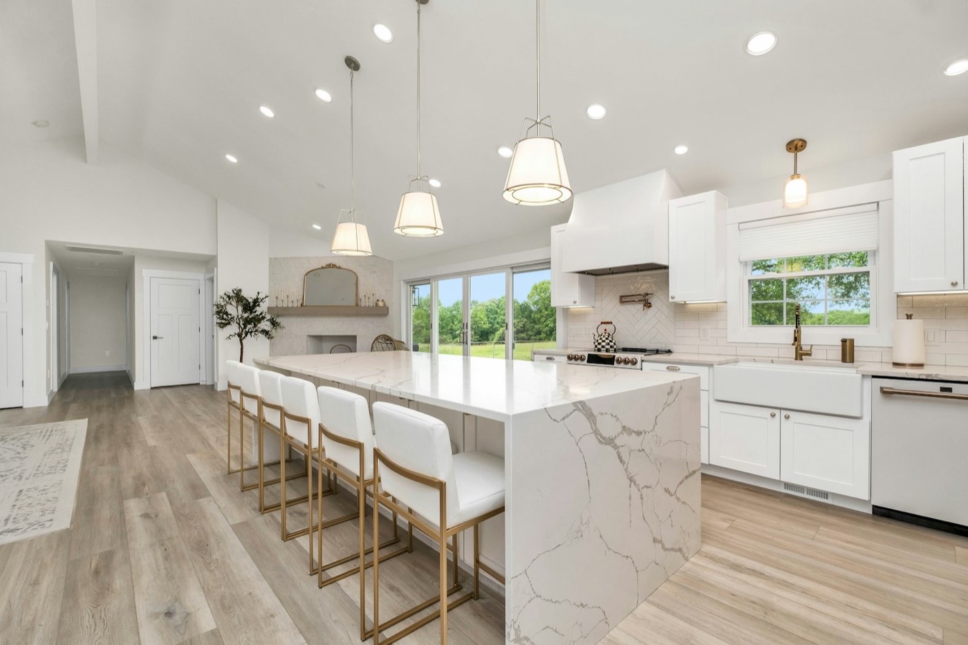A finished kitchen with white cabinets, a marble island and pendant lights